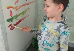 CHłopiec maluje linie poziome na dużym papierze.